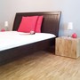 Teakholz Bett aus Massivholz in der MOEBEL KOLONIE Holz Farbe Rotbraun, Kissen in der Farbe rot als Accessoires, ein Meisterstueck in Schreiner Qualitaet aus unserer Manufaktur, Massivholz Teakholz Moebel Muenchen