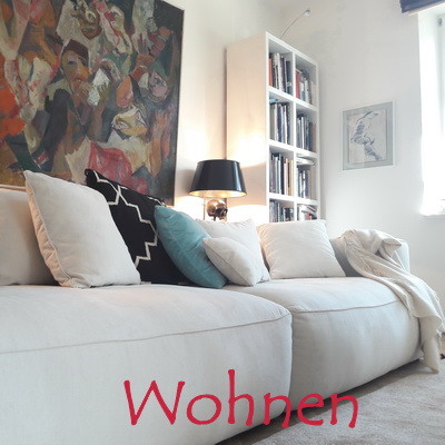Bild mit großem Lounge Sofa von Sits mit hellem Stoffbezug im Wohnzimmer Ambiente mit Leuchten und Dekorationen Teppich und Bücherregal im Hintergrund